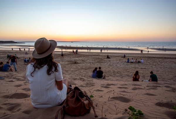 Woman sitting on the sand with her back to the camera at Mindil Beach at sunset, Darwin, Northern Territory © Tourism Australia