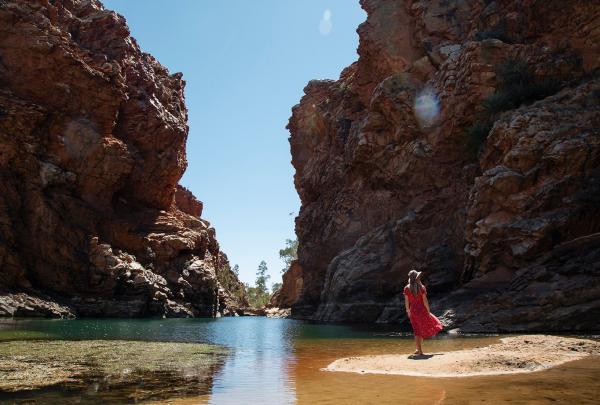 Woman in a red dress standing on a sandy bank at Ellery Creek Big Hole, West Macdonell Ranges, Northern Territory © Tourism Australia