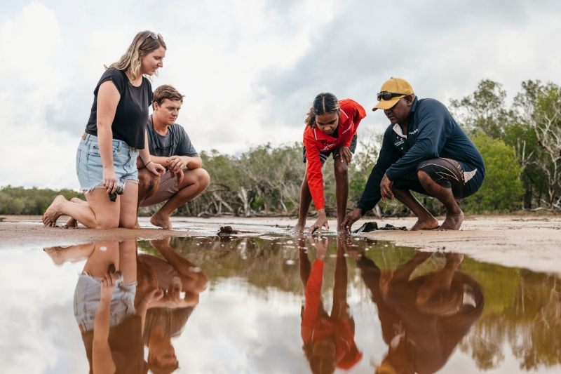 Indigenous tour guides and couple kneeling down to view a tidal pool, Southern Cross Cultural Walk, Cygnet, Western Australia © Tourism Australia