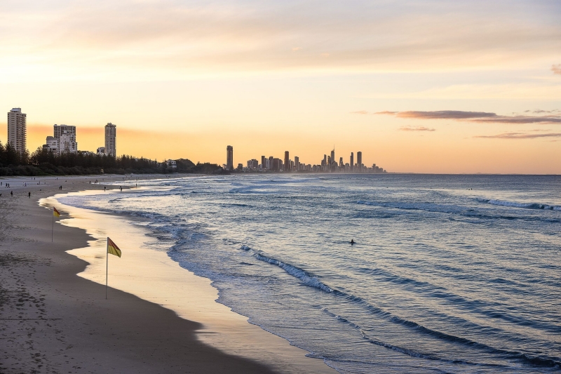 As the sun sets, the sky glows with a warm blend of oranges and pinks, casting a serene light over the lapping waves of Burleigh Heads on the Gold Coast, Queensland © Tourism Australia
